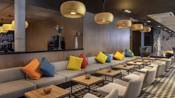 A modern lounge area with a sofa, chairs, tables, and hanging lights.