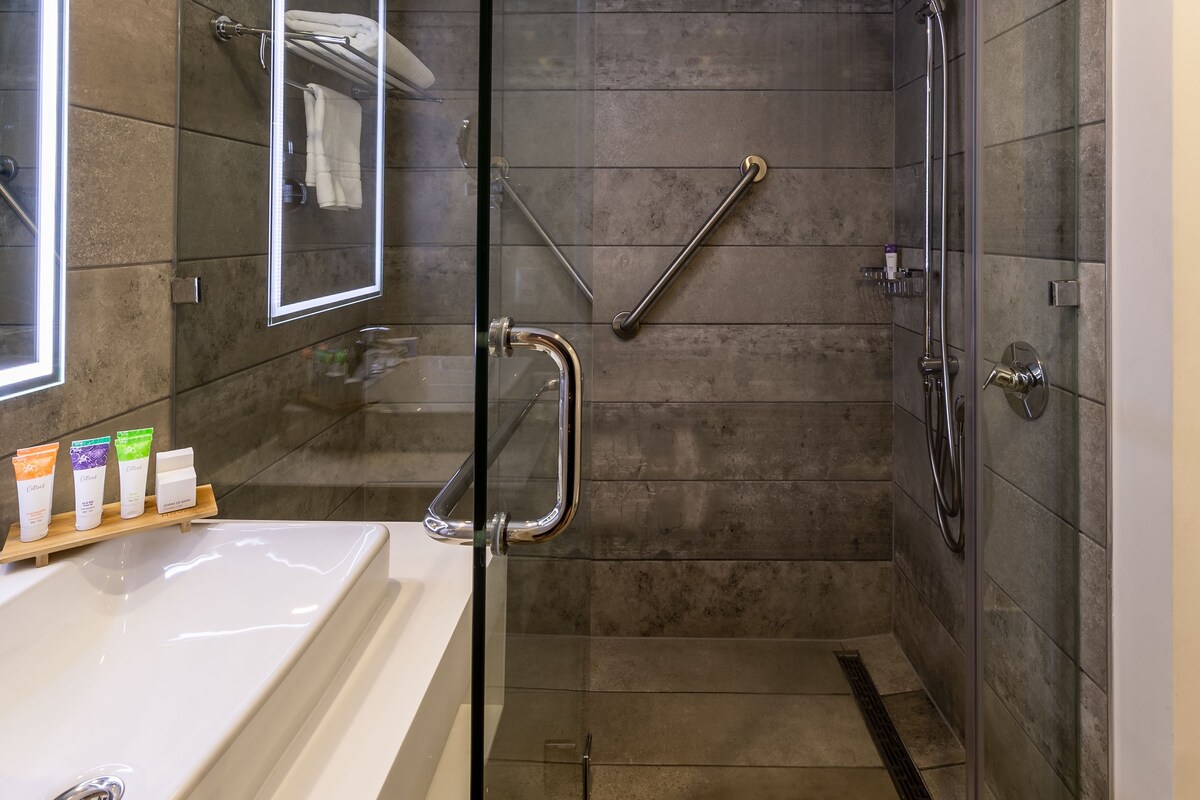A modern bathroom with a glass-enclosed shower, a vanity with a large mirror, and a selection of toiletries on a tray.