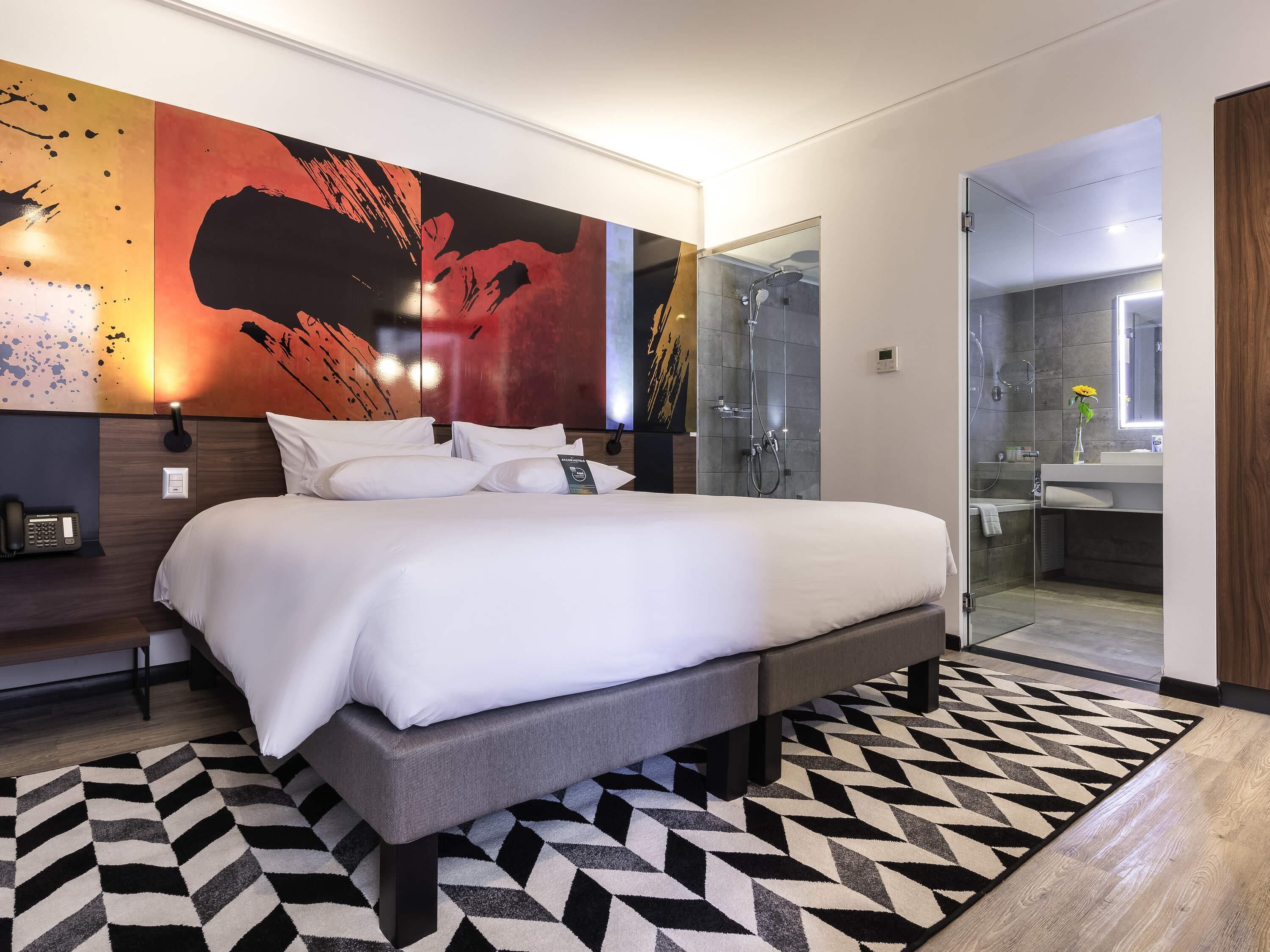 Une chambre d’hôtel moderne dotée d’un grand lit, d’un espace douche et d’une salle de bain avec un miroir.