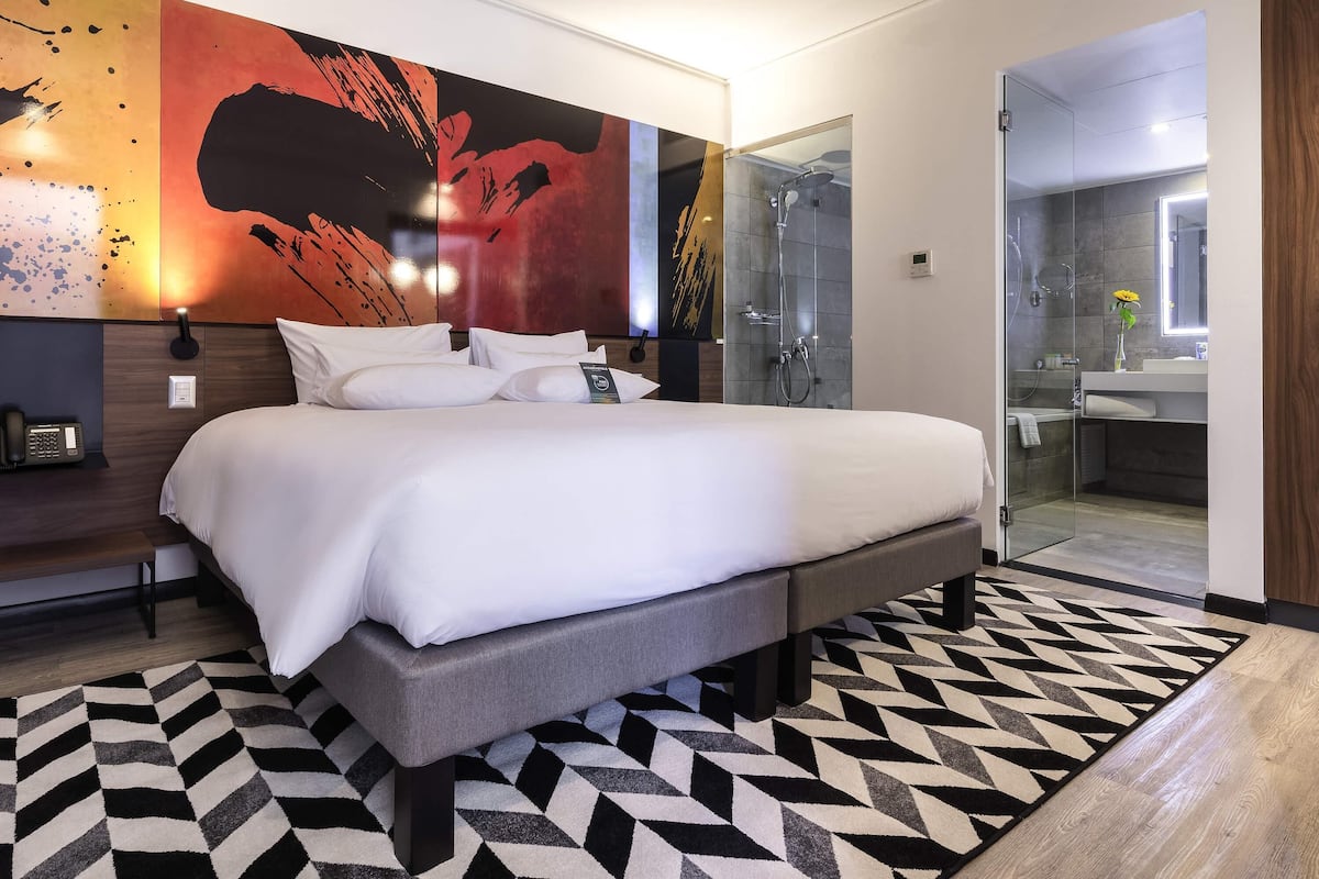 Une chambre d’hôtel moderne dotée d’un grand lit, d’un espace douche et d’une salle de bain avec un miroir.