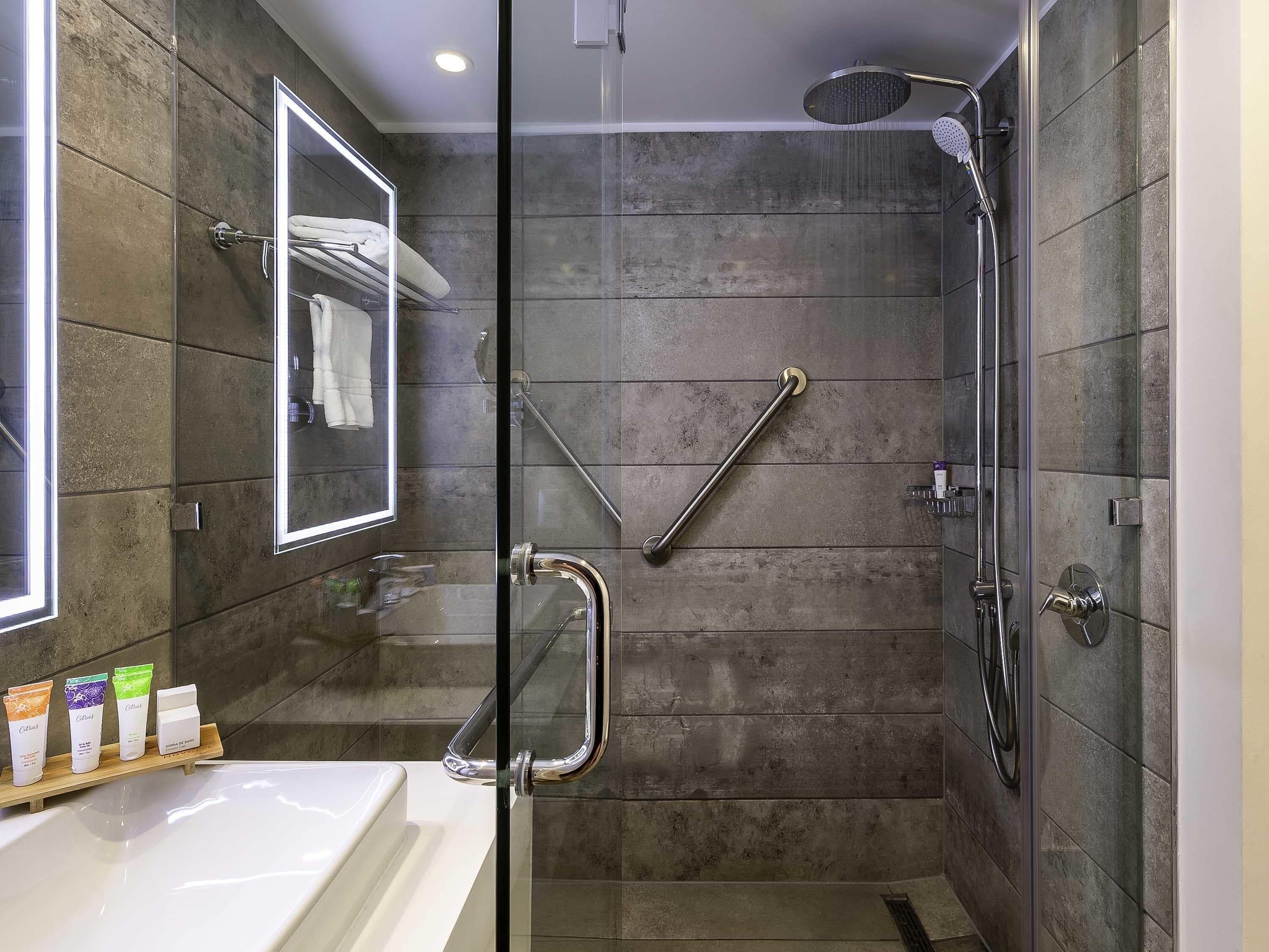 A modern bathroom with a glass shower enclosure, a handrail, a glass-enclosed sink, and a mirror.