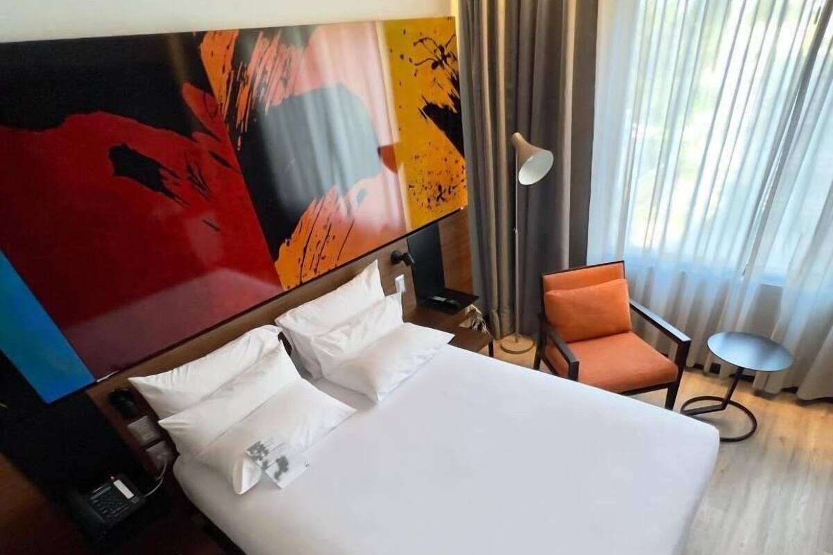 Une chambre d’hôtel avec un grand lit, une chaise, une petite table et un tableau au mur.