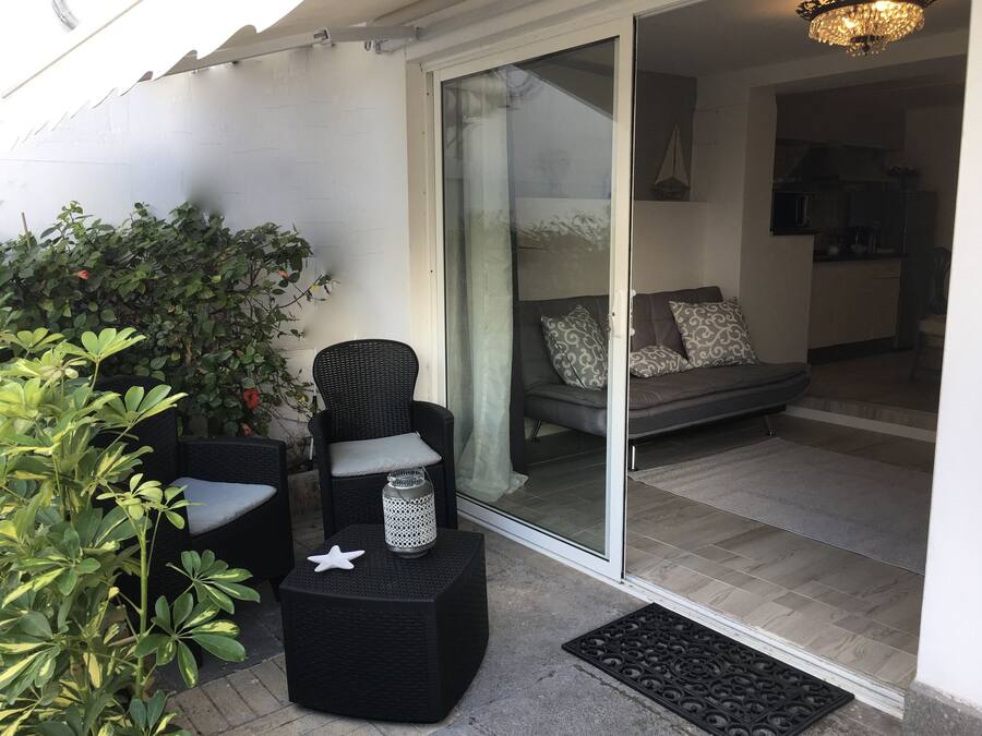 A modern outdoor seating area with wicker furniture, a glass door leading to a living room, and a small decorative plant.