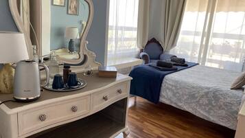 A bedroom with a bed, a dresser with a mirror, a bedside table with a lamp, and a window with curtains.