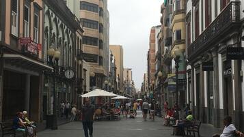 Calle flanqueada por edificios, algunos con letreros y anuncios. Hay bancos y gente caminando o sentada.