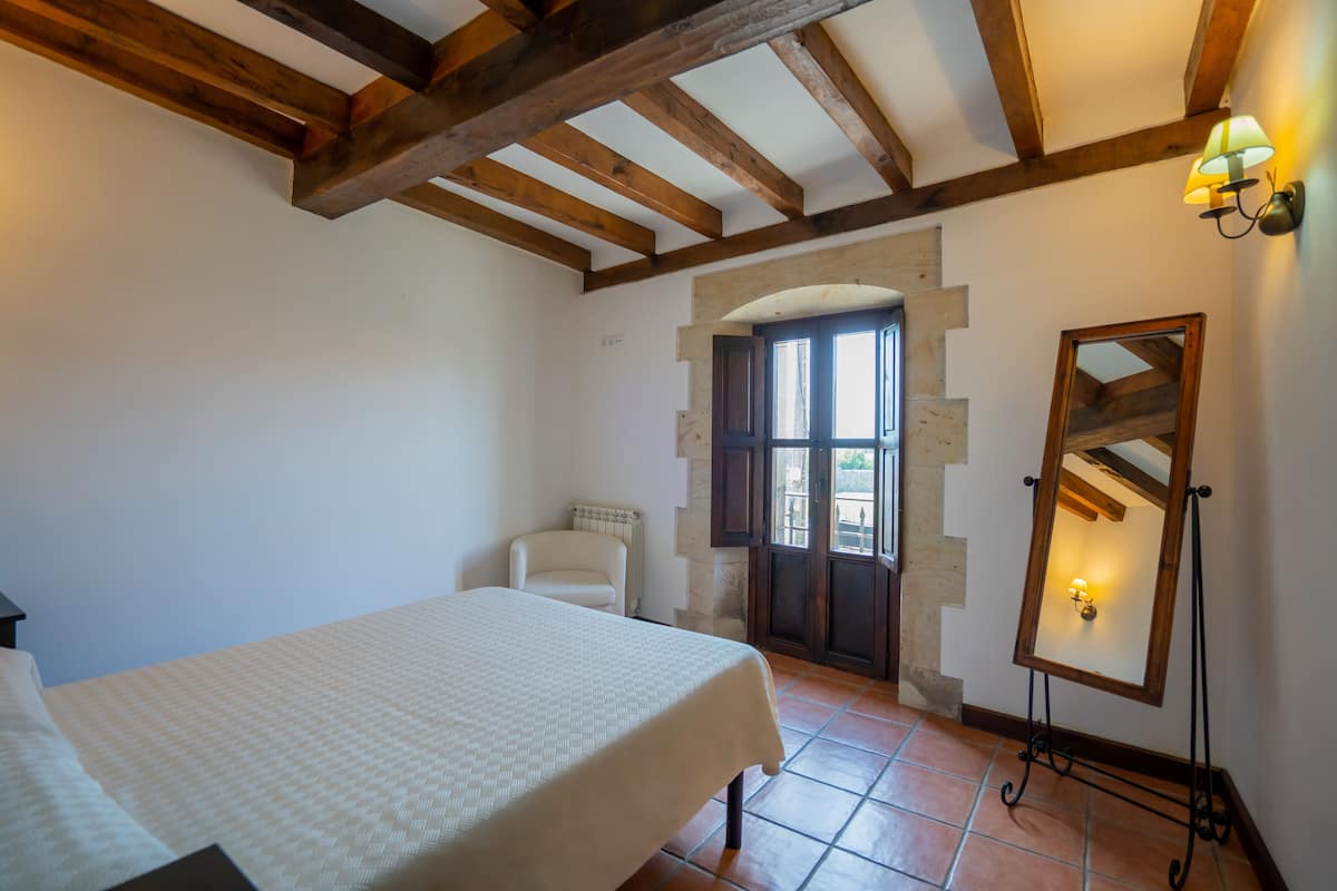 Ein Schlafzimmer mit Bett, einem Sessel, einem Spiegel und einer Tür, die zu einem Außenbereich führt.