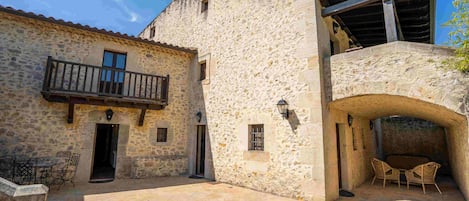 A stone building with a balcony and an archway leading to a covered patio area.