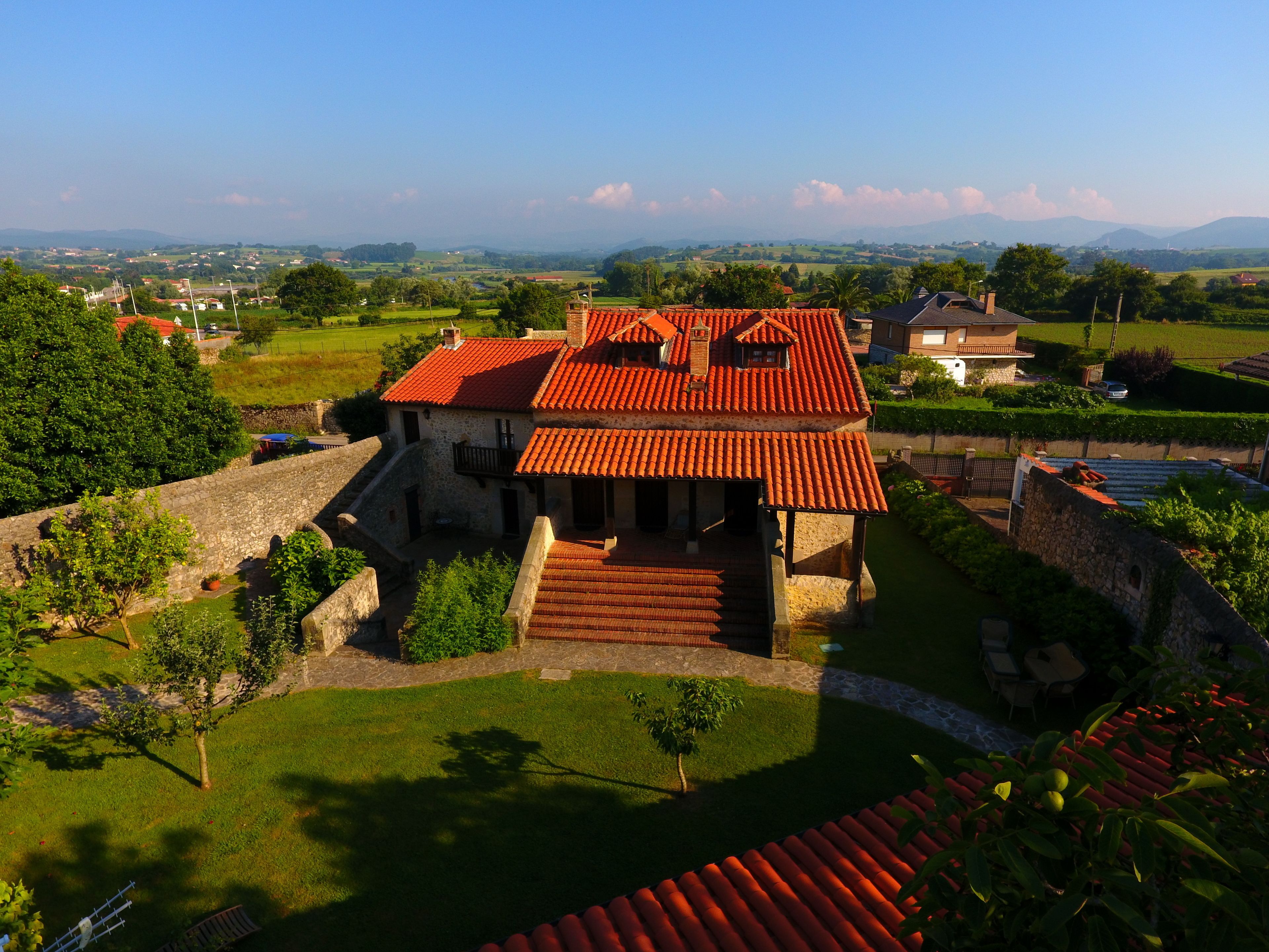 A historic building with a red-tiled roof, stone walls, and a courtyard with a small tree.