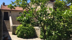 Un bâtiment en pierre avec un toit en tuiles, un escalier menant à une porte et une végétation luxuriante.