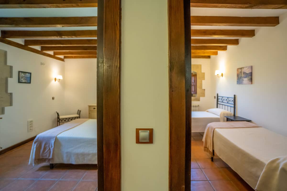 Ein Zimmer mit zwei Betten, Holzbalken an der Decke, einer Wandleuchte und einem kleinen Gemälde.