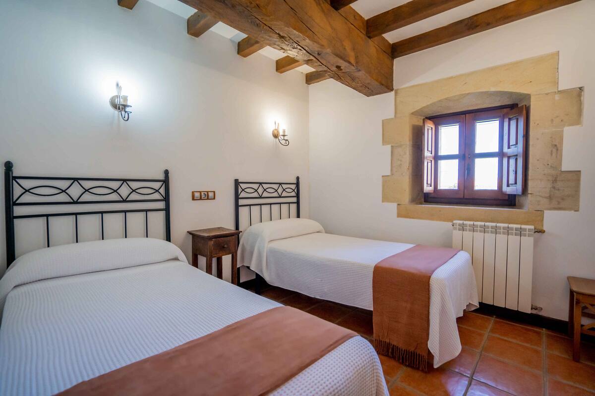 Ein Zimmer mit zwei Betten, einem Fenster mit Rollläden und einer Holzbalkendecke.