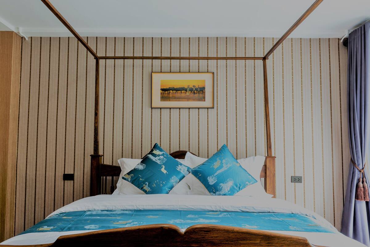 Een net opgemaakt bed met een blauw-witte dekbedovertrek, een lijst met een afbeelding erboven en een houten hoofdbord.