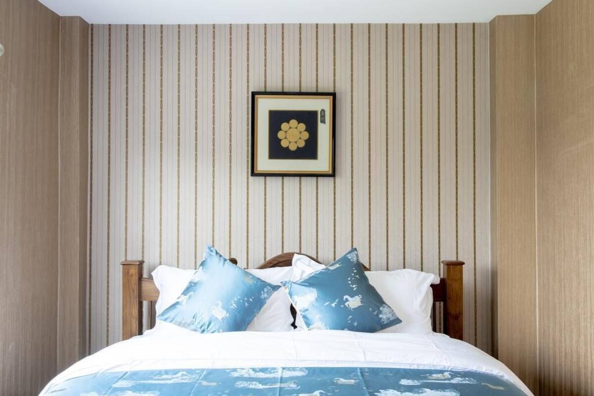 Een slaapkamer met een bed, kussens en een lijst met een foto aan de muur.