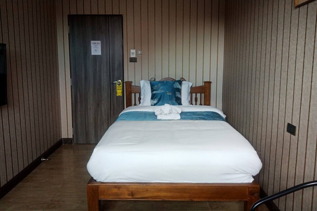 Een eenpersoonsbed met houten frame, witte beddengoed en een blauw kussen.