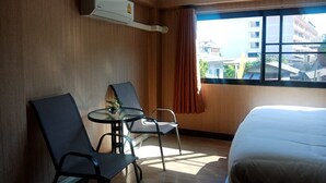 Une chambre d’hôtel avec un lit, deux chaises, une petite table et une fenêtre avec des rideaux.