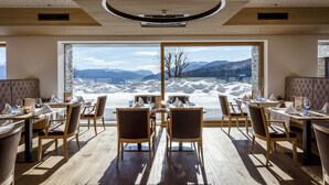 Een restaurant met houten vloeren, ronde tafels en stoelen, met een groot raam dat uitzicht biedt op een berg.