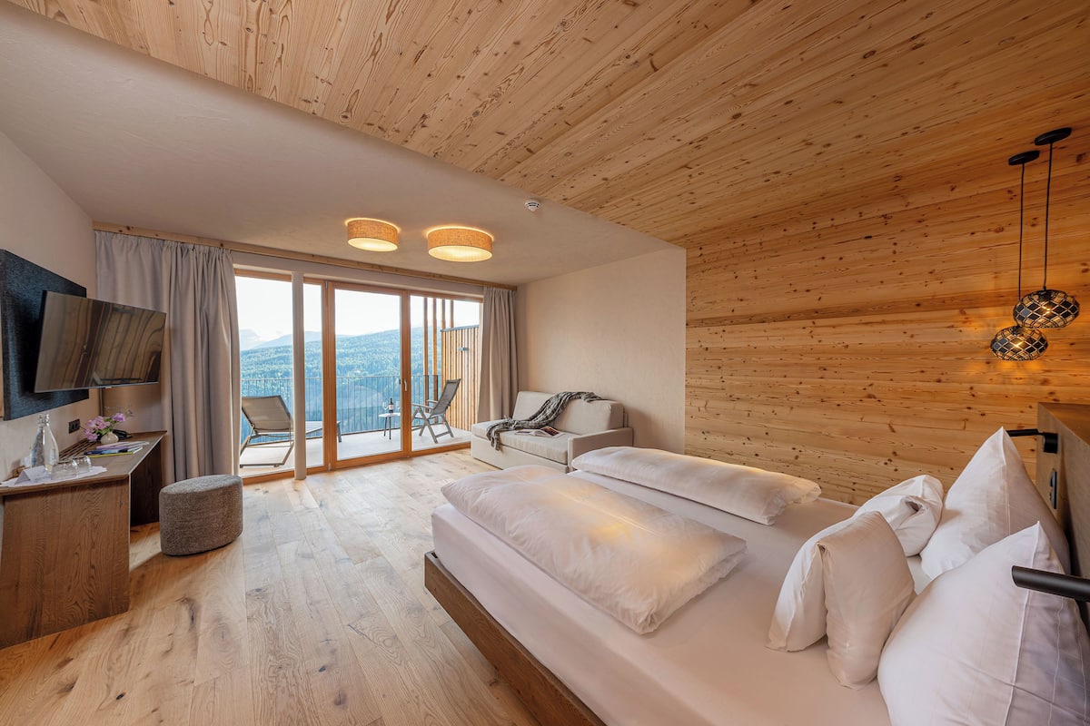 Une chambre moderne avec un plafond en bois, un grand lit, une télévision et un balcon offrant une vue agréable.