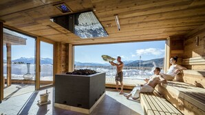 Een sauna met houten banken, een stenen openhaard en grote ramen met uitzicht op de bergen.