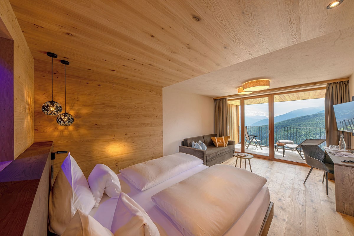 Une chambre avec un grand lit, un bureau, une chaise, un canapé et un balcon avec vue.