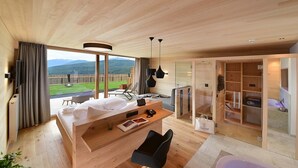 Een moderne hotelkamer met een groot bed, een bureau, een stoel en uitzicht op een groen landschap door grote ramen.