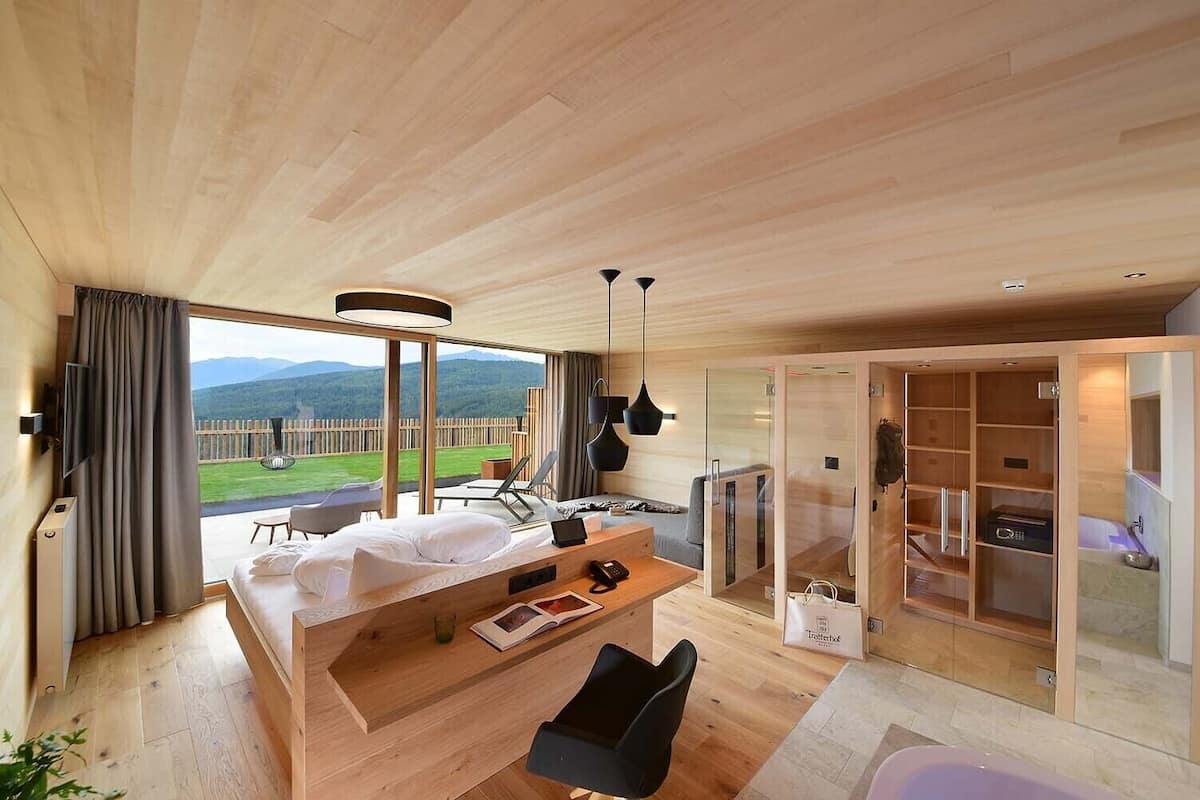 Une chambre d’hôtel moderne dotée d’un grand lit, d’un bureau, d’une chaise et offrant une vue sur un paysage verdoyant grâce à de grandes fenêtres.