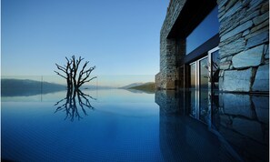 A modern building with stone walls and a glass pool reflecting a tree and mountains. - Tratterhof Mountain Sky Hotel (Rio di Pusteria)