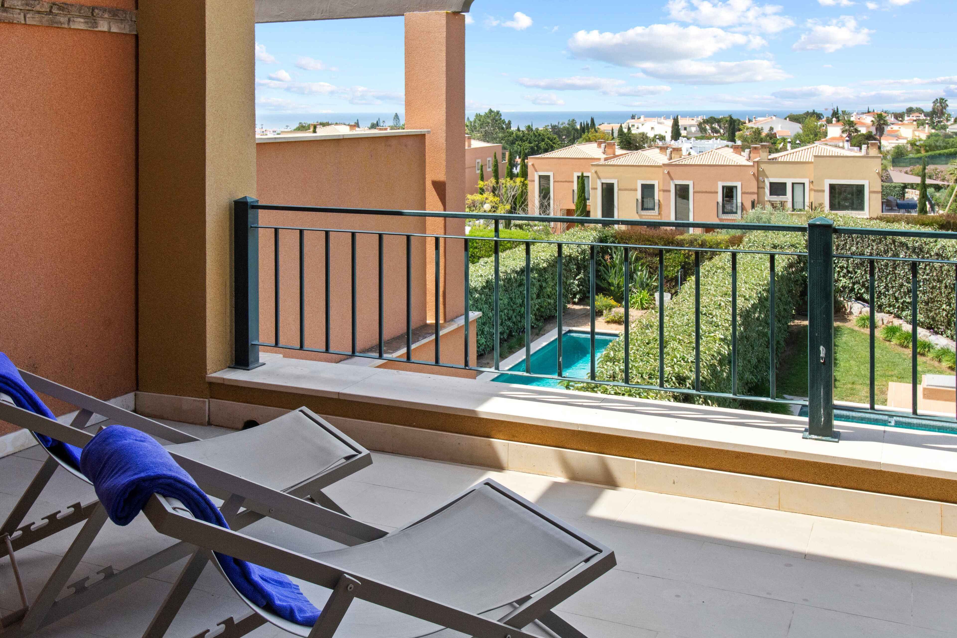 A balcony with two sun loungers, a pool, and a view of residential buildings.