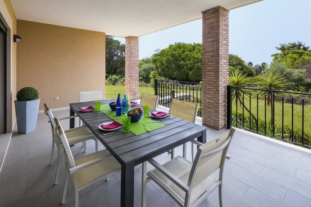 A covered patio with a table set for four, surrounded by chairs, and a view of a landscaped garden.