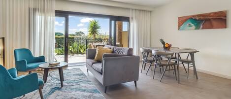 Una sala moderna con sofá, sillas, una mesa de comedor y un ventanal con vistas a zonas verdes y una palmera.