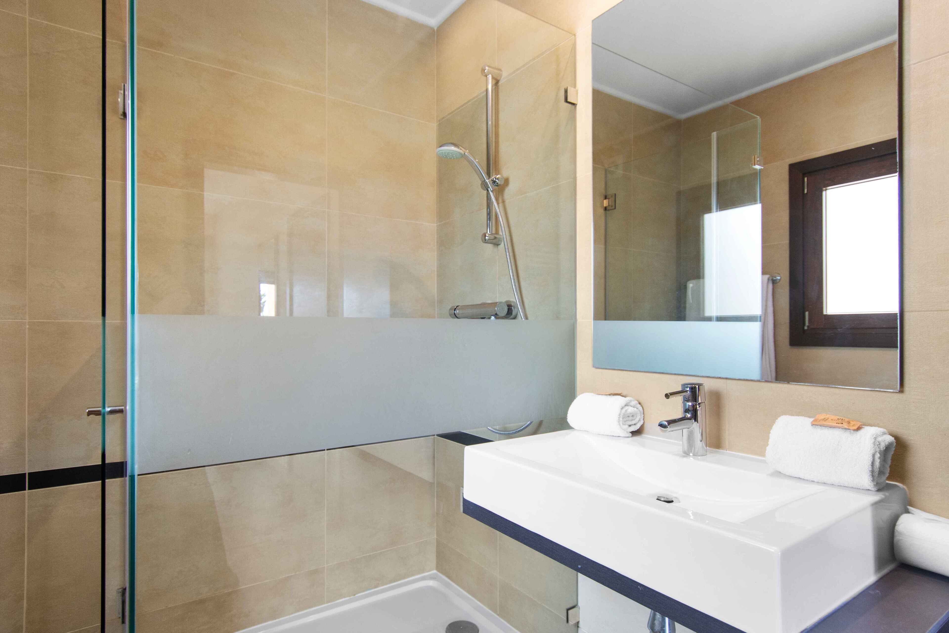 A modern bathroom with a glass shower enclosure, a white sink with a towel, and a large mirror.