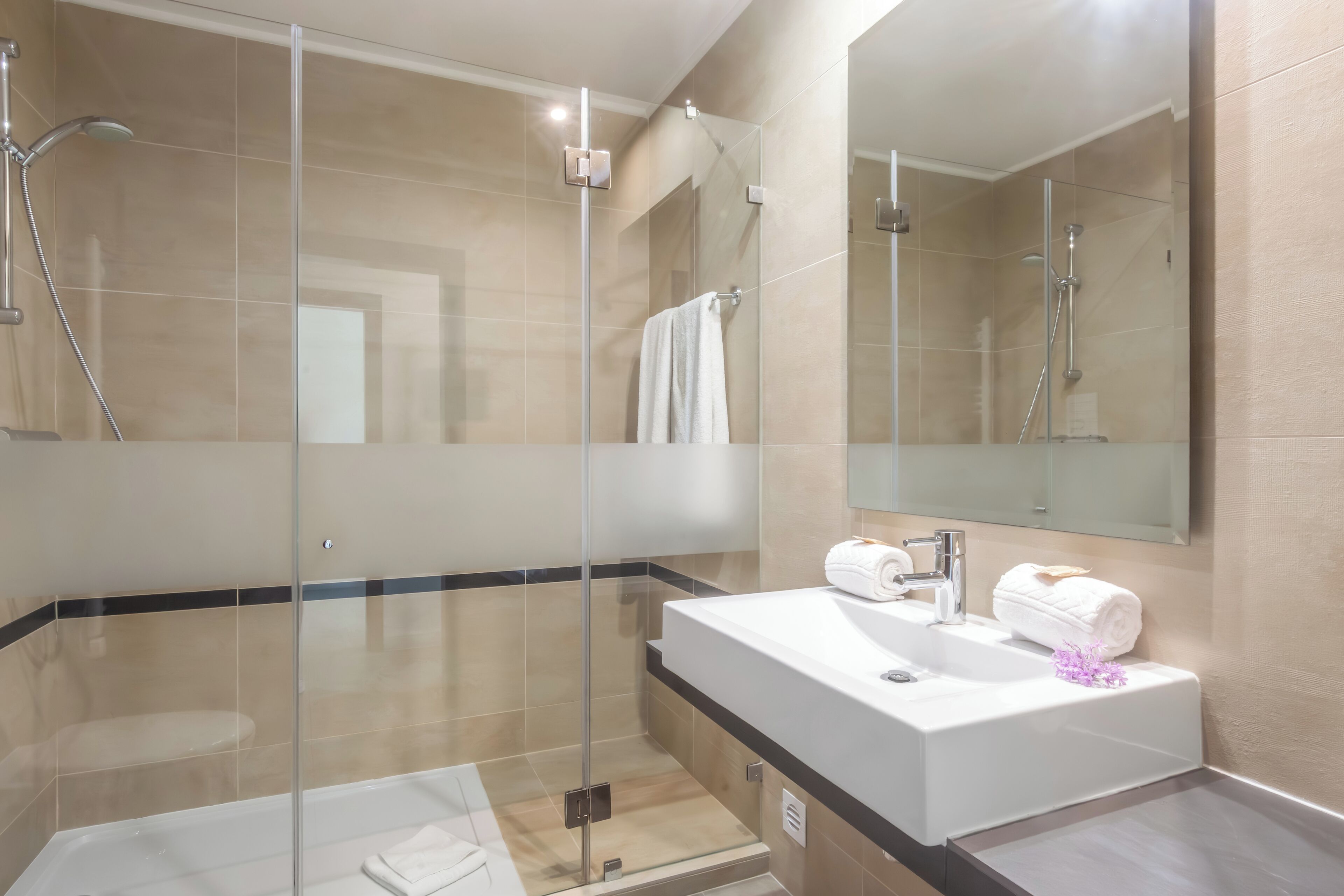 Un baño moderno con ducha envuelta en vidrio, un lavamanos blanco y un espejo grande.