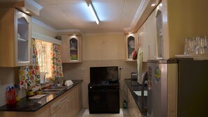 A compact kitchen with wooden cabinets, a black stove, and a refrigerator. - Kifaru House - Karen (Nairobi)