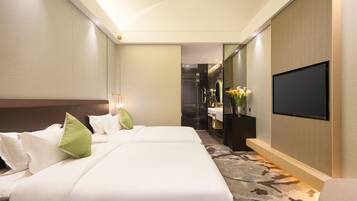 Ein Hotelzimmer mit einem großen Bett, einem an der Wand befestigten Fernseher und einem durch eine Glastür einsehbarer Badezimmer.