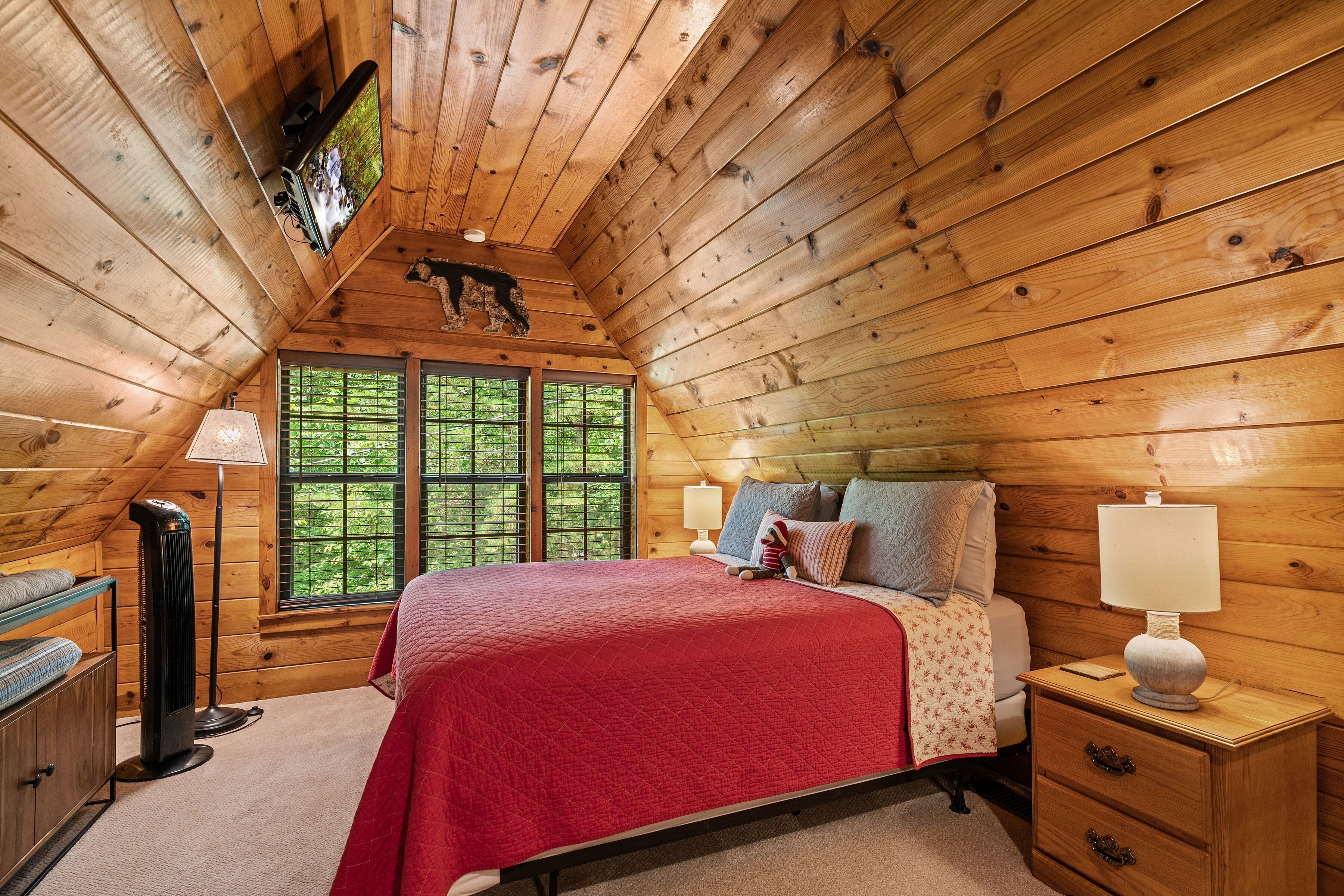Ein gemütliches Schlafzimmer in einer Holzhütte mit einem großen Bett, einem Nachttisch mit Lampe, einem Heizkörper und einem Fenster mit Blick auf den Wald.