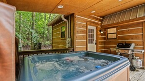 A wooden cabin with a hot tub, a grill, and a door leading to a small cabin.