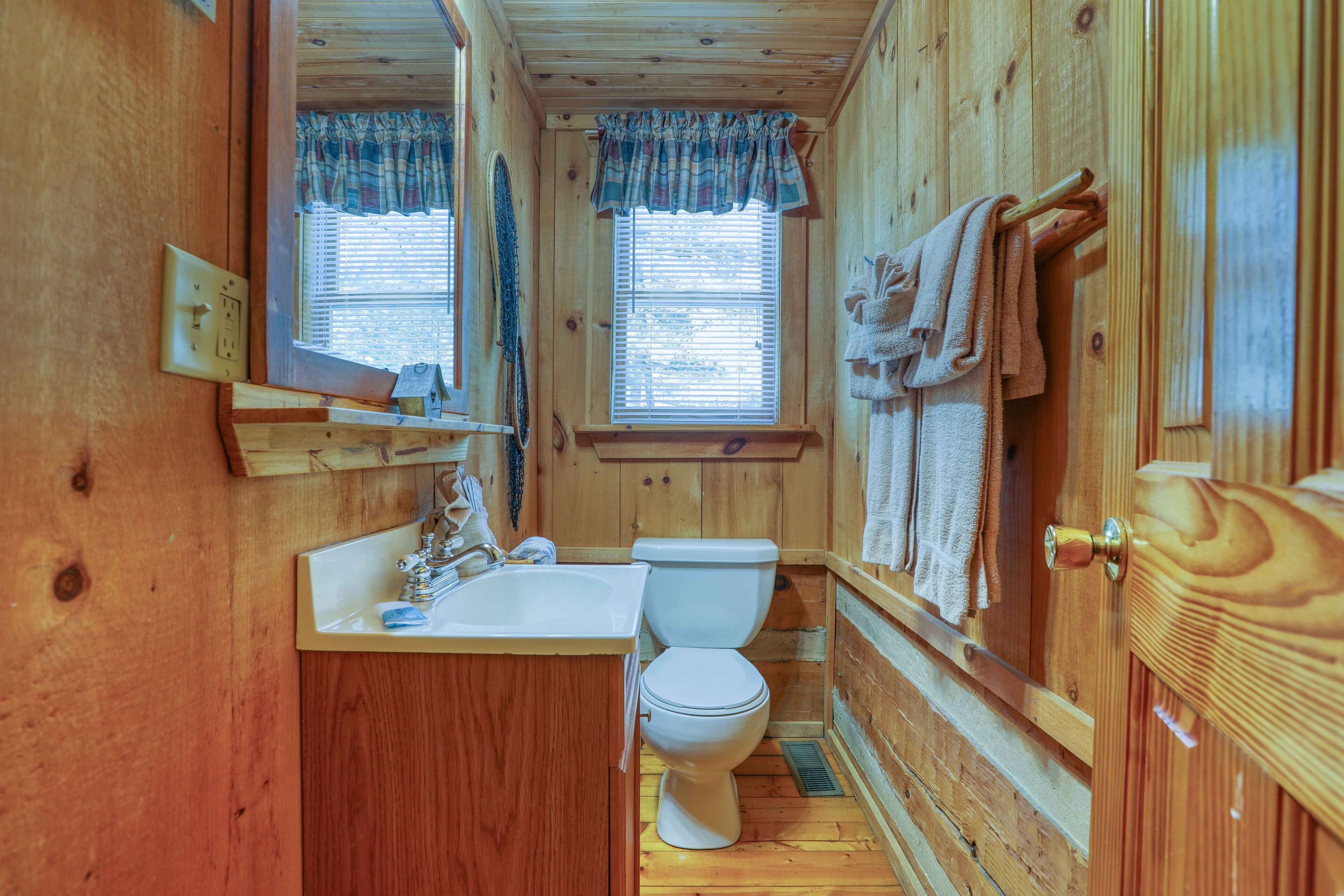 A wooden cabin bathroom with a toilet, sink, and window.