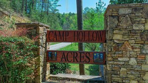 Un letrero de madera con la inscripción 'Camp Hollow Acres', sujeto a una pared de piedra.