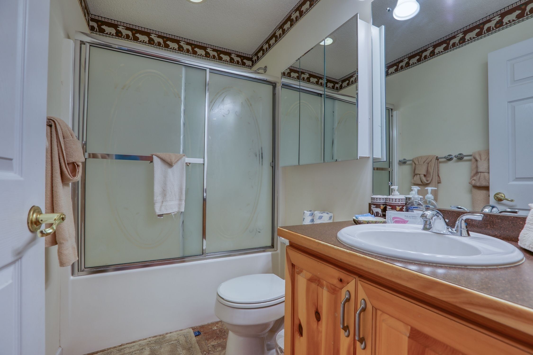 Un baño con cabina de ducha de vidrio, inodoro blanco, tocador de madera con lavamanos y un espejo grande.