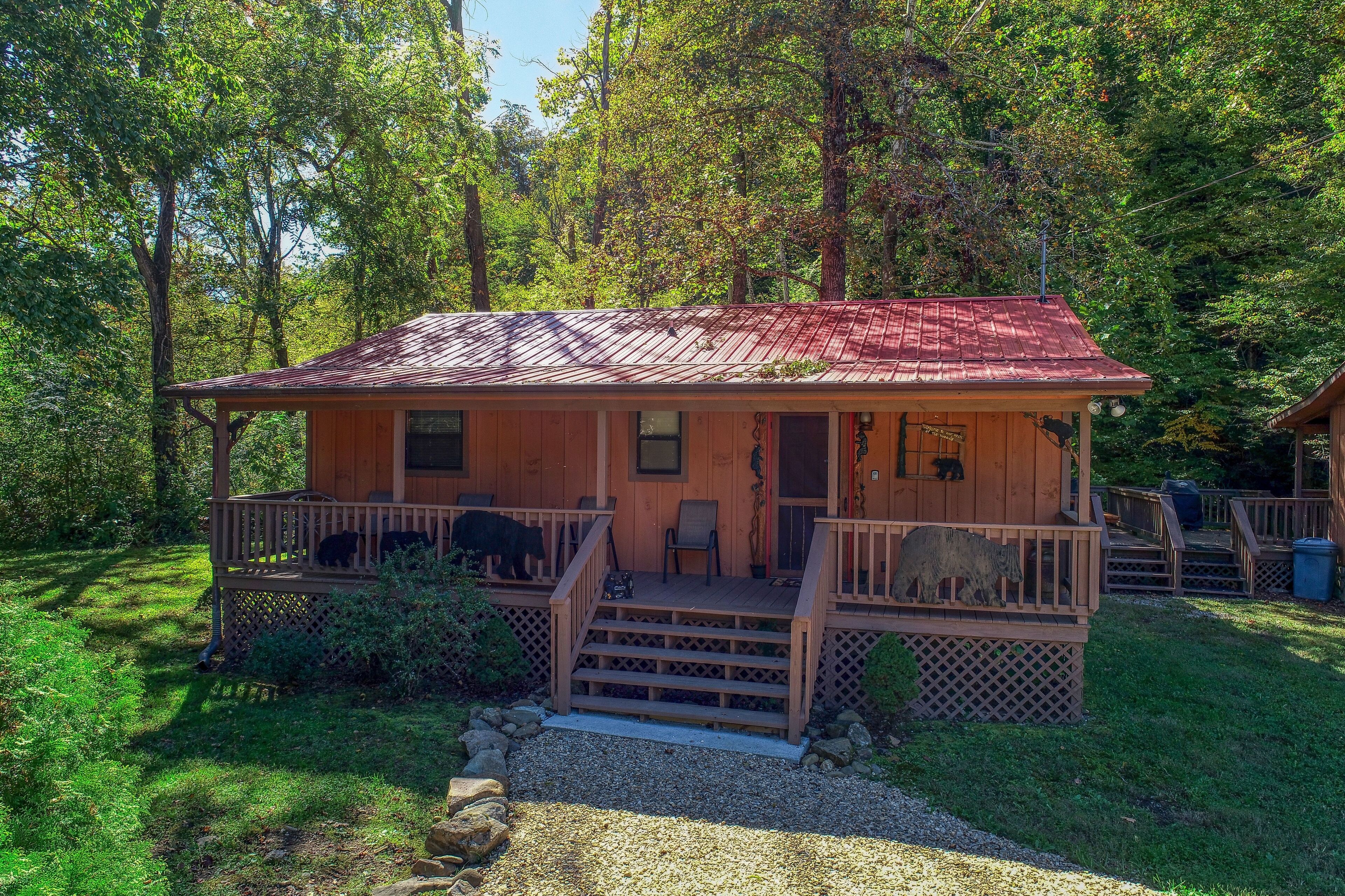 A wooden cabin with a red roof, a porch with chairs, and a bear statue.