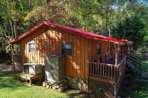 Una cabaña de madera con techo rojo, un porche y cimientos de piedra.