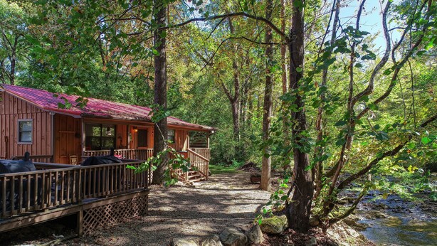 A rustic cabin with a wooden deck and a covered porch, surrounded by a forested area with a stream. - Wandering Creek - 2 Bedrooms, 1 Baths, Sleeps 6 Cabin by RedAwning (Cosby)