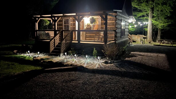 A wooden cabin with a porch, stairs, and a well-lit interior. - Sweet - 2 Bedrooms, 2 Baths, Sleeps 6 Cabin by RedAwning (Cosby)
