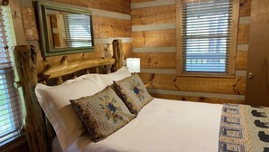 A wooden log cabin bedroom with a bed, two pillows, a mirror, and two windows with blinds. - Sweet - 2 Bedrooms, 2 Baths, Sleeps 6 Cabin by RedAwning (Cosby)