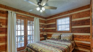 Un dormitorio de cabaña de madera con cama, cortinas, ventilador de techo y ventana.