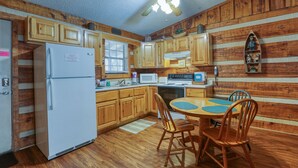 Una cocina tipo cabaña con armarios de madera, un refrigerador, un microondas y una mesa de comedor con sillas.