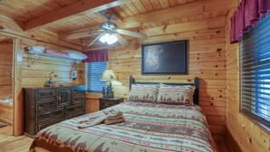 Ein Schlafzimmer in einer Holzhütte mit Bett, Schminktisch und Deckenventilator.