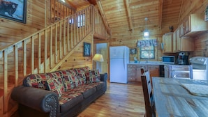 Ein Holzblockbau-Innenraum mit Sofa, Esstisch, Küchenzeile und einer Treppe.