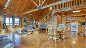 A spacious wooden cabin with a living area featuring a sofa, chairs, and a dining table. A staircase leads to an upper level, and the kitchen area is visible. - Mountain View - 2 Bedrooms, 2 Baths, Sleeps 6 Cabin by RedAwning (Cosby)