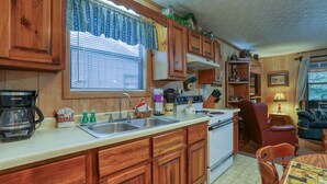 A kitchen with wooden cabinets, a stove, a sink, and a dining area with a table and chairs.