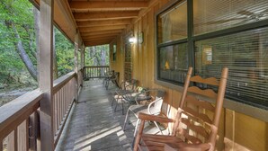 A covered porch with wooden railings, a row of chairs, and a view of the surrounding forest.